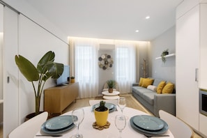A modern living room with a sofa, a dining table set, and a television on a wooden cabinet.