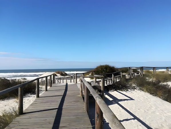Une promenade en bois menant à la plage, d’où l’on a une vue dégagée sur l’océan.