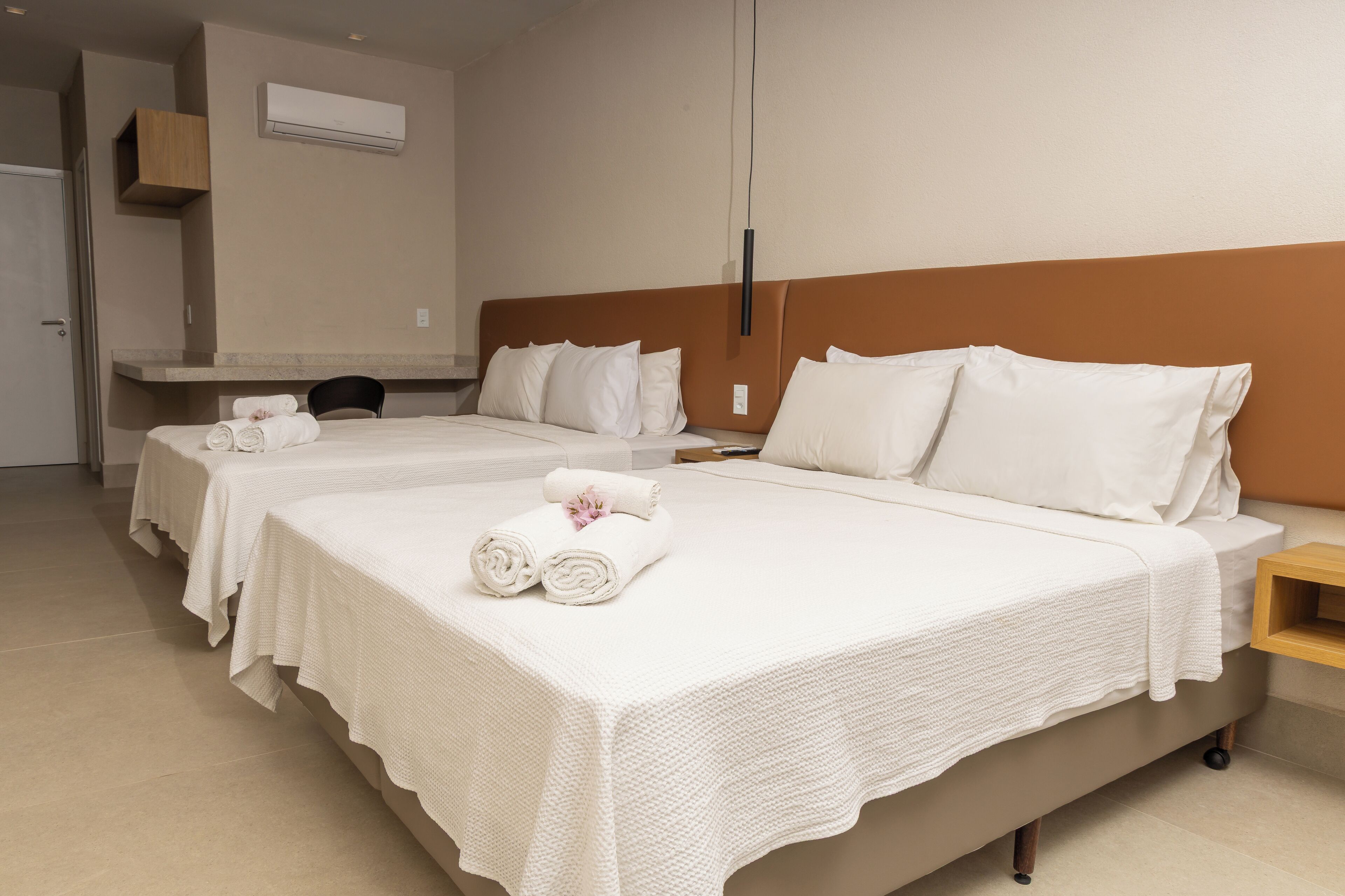 A hotel room with two beds, each with white linens and pillows, a wooden nightstand, and a wall-mounted air conditioning unit.