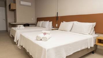 A hotel room with two beds, each with white linens and pillows, a wooden nightstand, and a wall-mounted air conditioning unit.