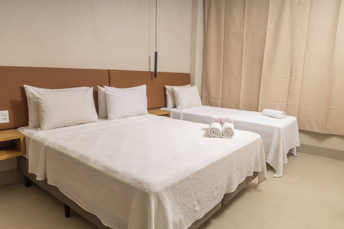 A hotel room with two beds, each with white linens and pillows, a wooden headboard, and a small bedside table with a lamp.