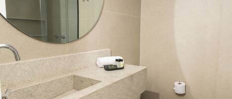 A bathroom with a granite sink, a mirror, a toilet, and a towel dispenser.