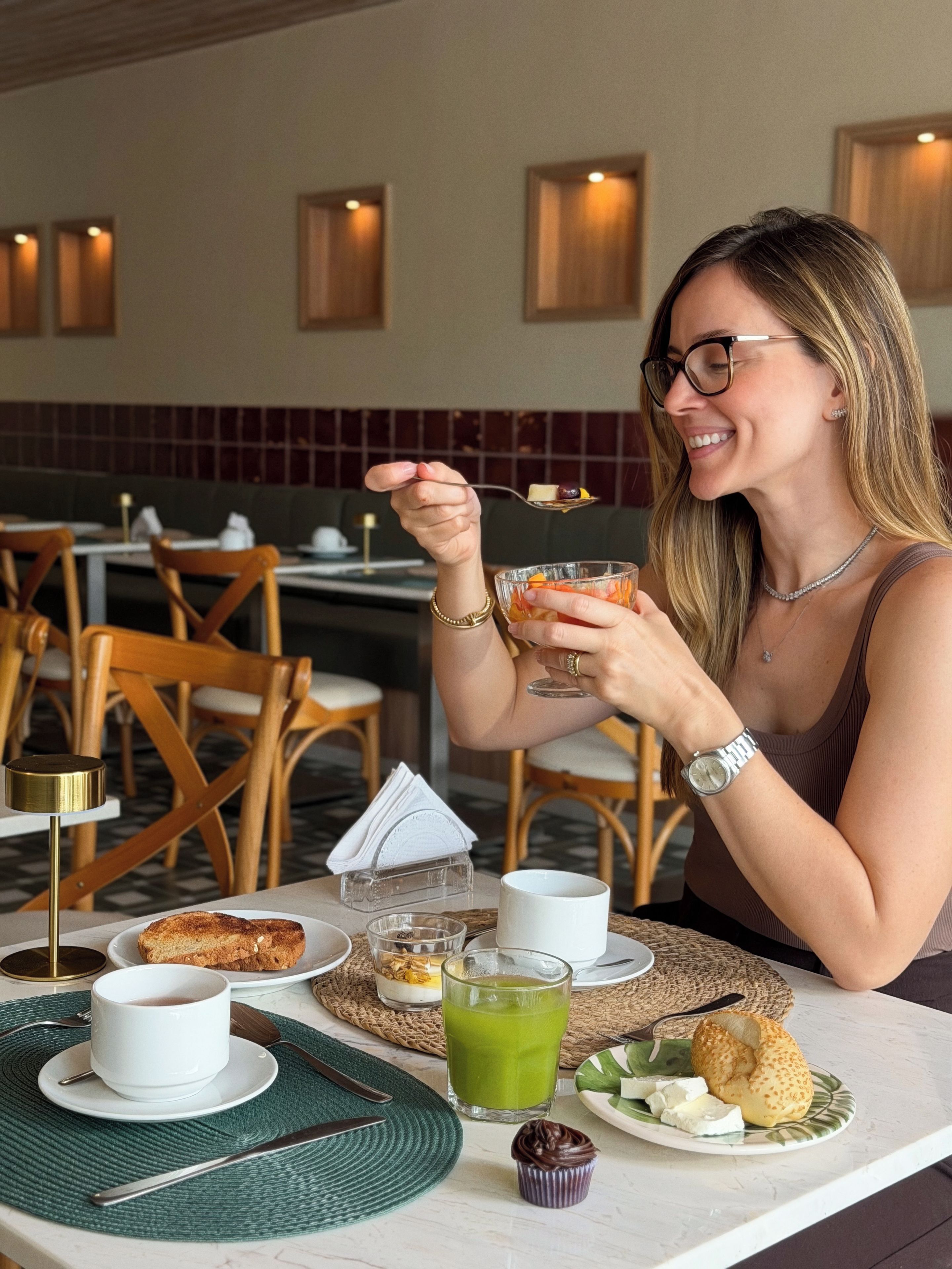 A person seated at a table with a meal consisting of toast, a green beverage, and a small dessert, with a napkin holder and a cup of tea visible.