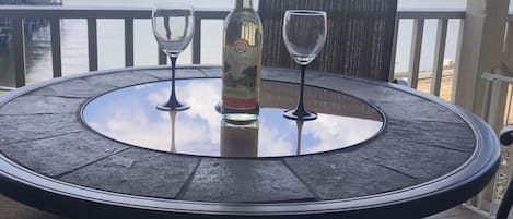 Uma mesa redonda com uma garrafa e duas taças numa varanda com vista para uma ponte.