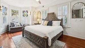 Une chambre avec un grand lit, un ventilateur de plafond et une fenêtre avec des stores.