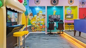 A room with a Simpsons-themed mural, gaming chairs, and a desk with a computer. - Luxury 6BR Near Universal, Pool, Spa & Game Room (Orlando)