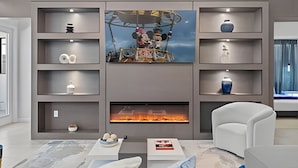 A modern living room with a fireplace, shelves with decorative items, and a large painting above the fireplace. - Luxury 6BR Near Universal, Pool, Spa & Game Room (Orlando)
