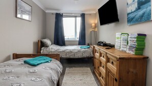 Un dormitorio con dos camas, televisor, escritorio con lámpara y ventana con cortinas.