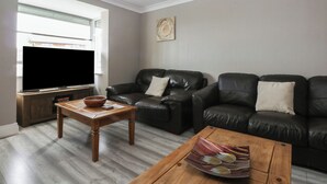 Una sala de estar con un televisor de pantalla plana, dos sofás de cuero, una mesa de centro de madera y una mesita auxiliar con un cuenco.
