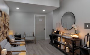 Ein modernes Interieur mit einer Sofagarnitur, einem Sessel, einer Holzwand, einem Spiegel und einem Tisch mit Kerzen.