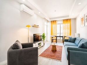 Un salon moderne avec un canapé, un téléviseur et un coin repas agrémenté de rideaux jaunes.