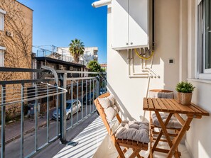Un balcon avec une table et des chaises en bois, un pot de fleurs et une vue sur la rue et les immeubles voisins.