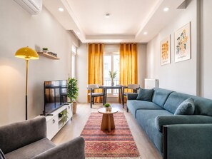 A modern living room with a sofa, chairs, a TV, a lamp, and a dining area with a table and chairs.