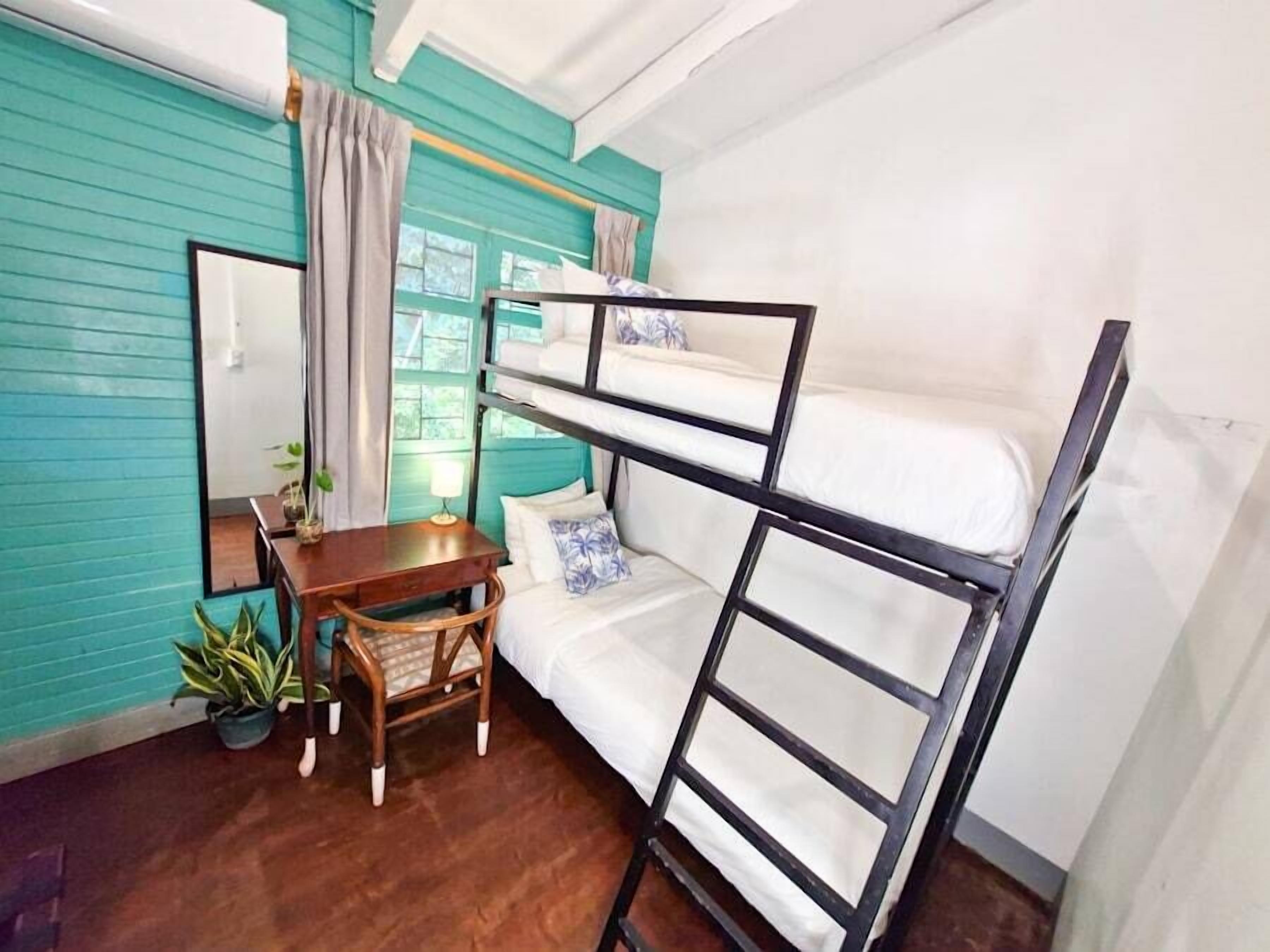 Habitación con literas, un escritorio de madera, un espejo y una ventana con cortinas.