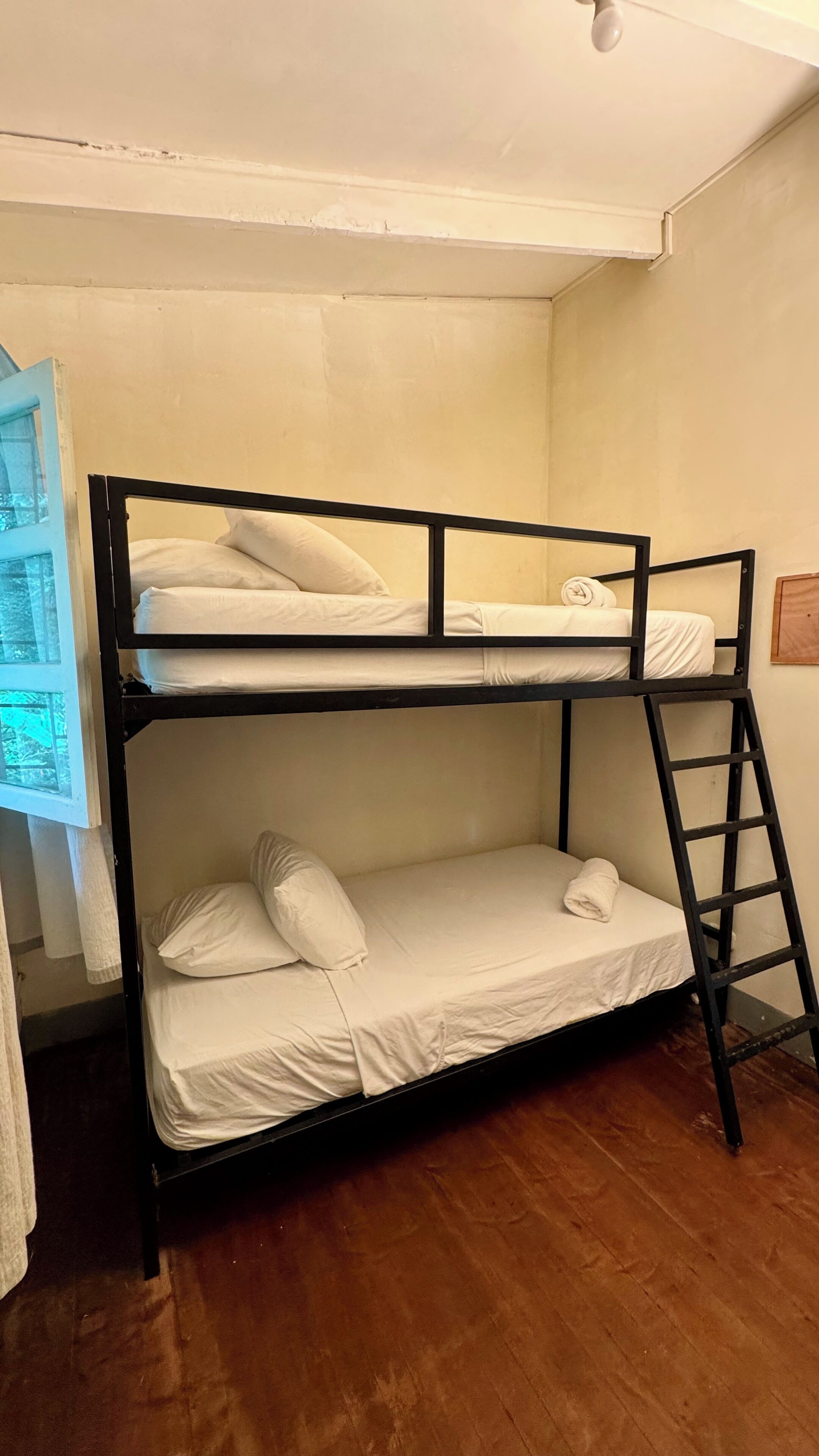 A bunk bed with white bedding in a room with wooden flooring and a white wall.