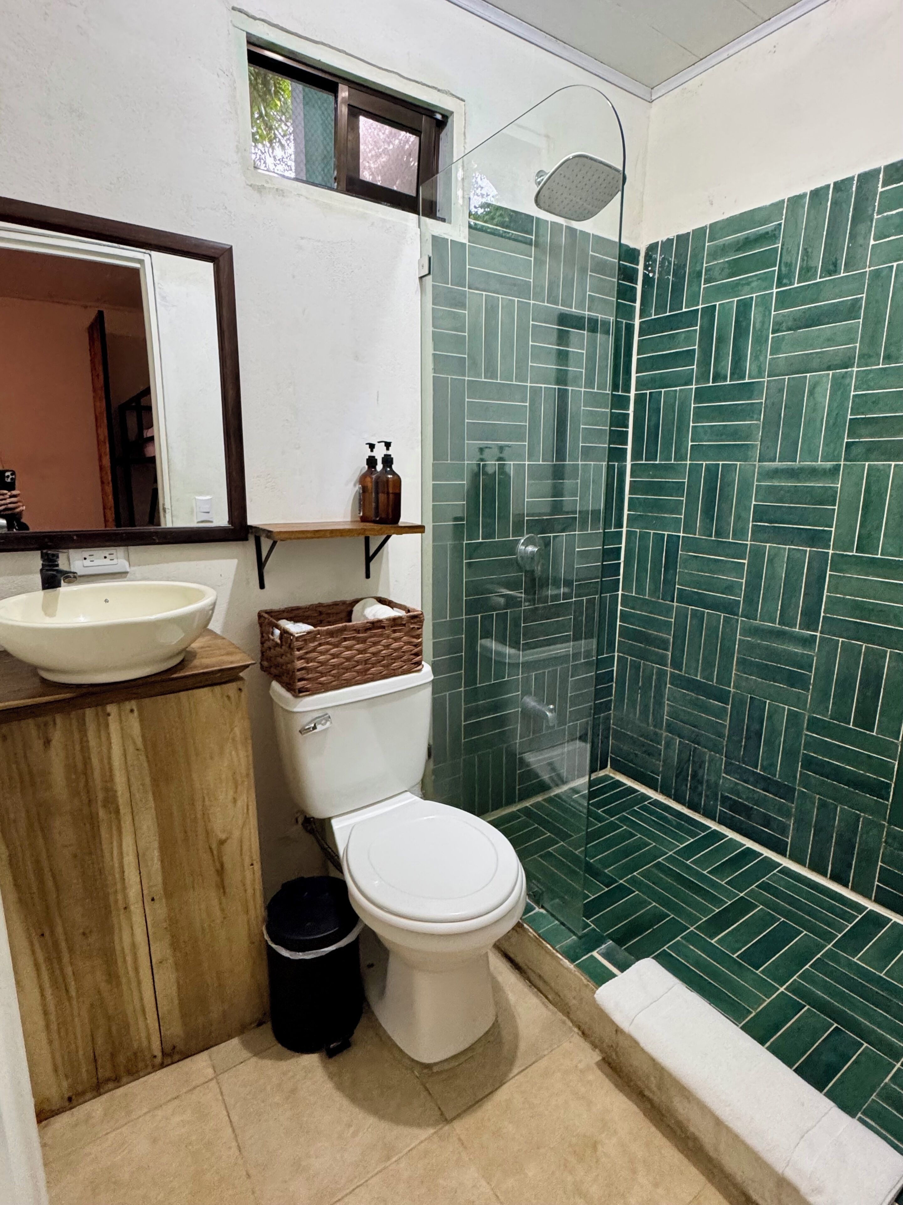 Une salle de bain avec un lavabo blanc, des toilettes et une douche aux carreaux verts.