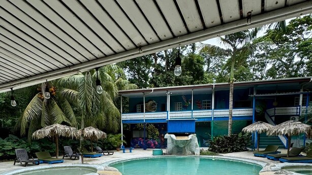 A pool area with lounge chairs, a water slide, and a building with a blue facade. - Agapi (Cahuita)