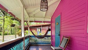 A covered porch with a hammock, a wooden chair, and a view of the outdoors. - Agapi (Cahuita)