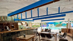 A restaurant with wooden tables and chairs, a bar area, and a view of an outdoor pool. - Agapi (Cahuita)