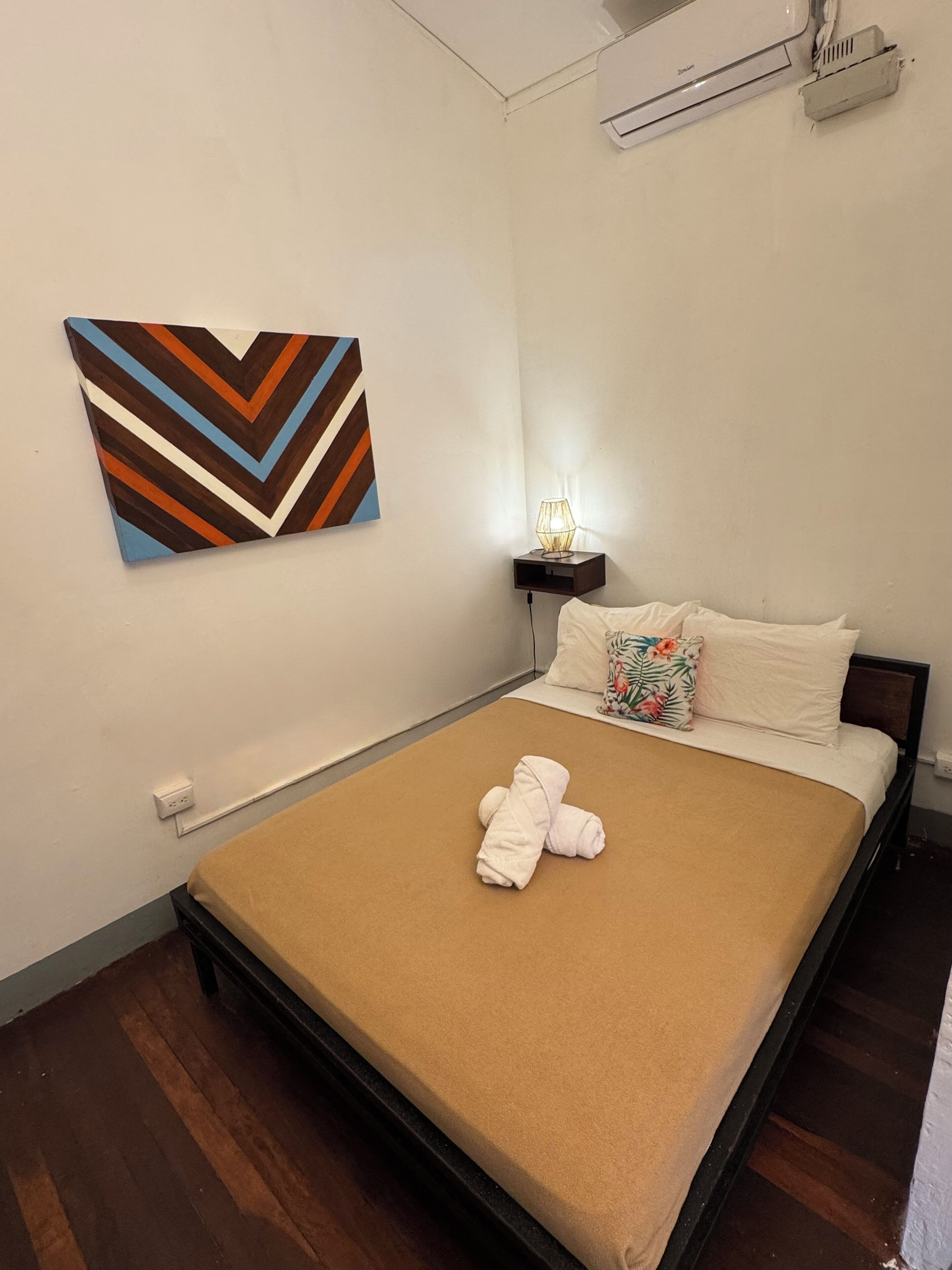 A bedroom with a bed, a wall-mounted light, a power outlet, and a decorative wall piece.