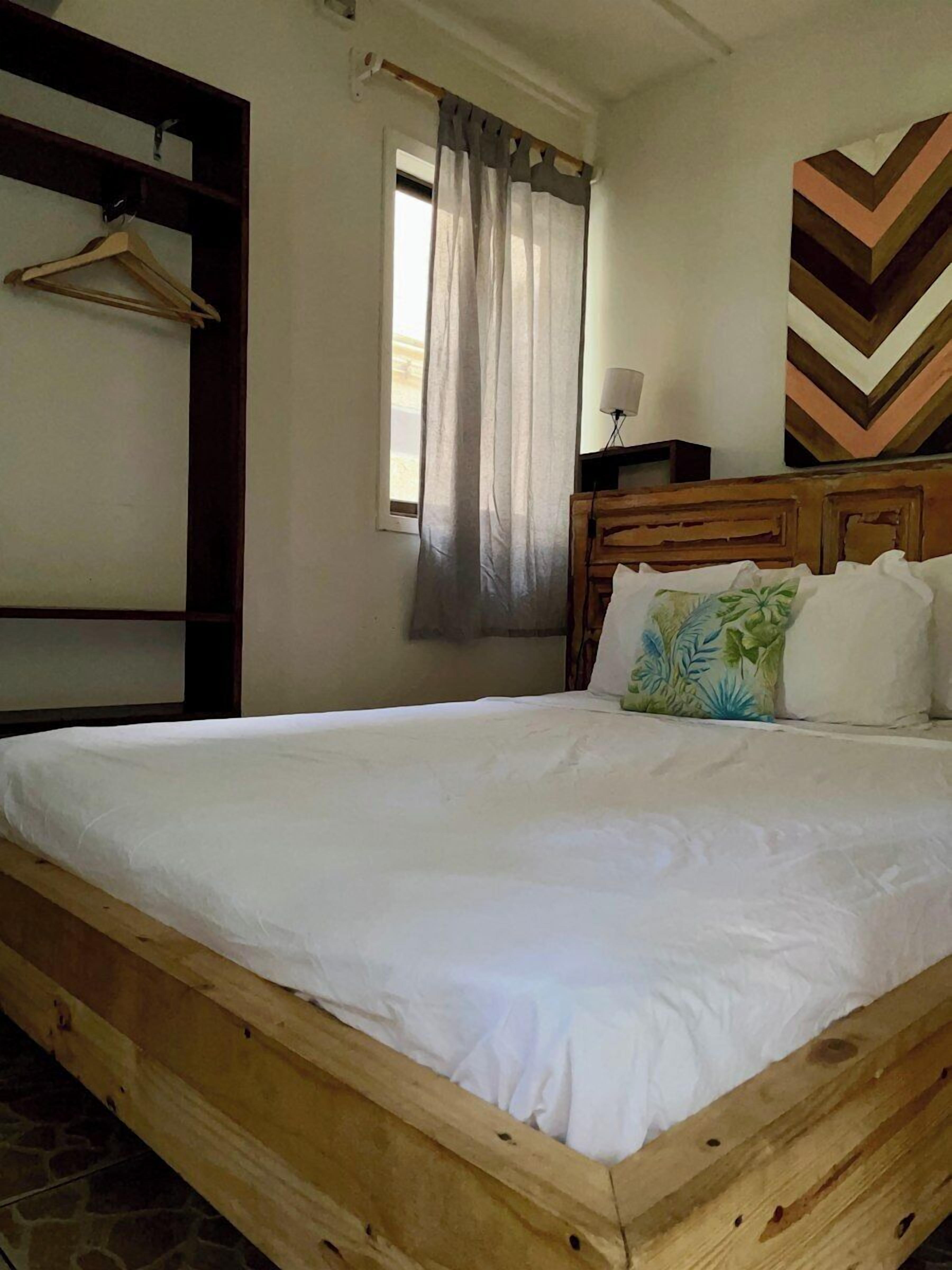 A wooden bed with white bedding, a wooden headboard, a wall-mounted lamp, and a chevron-patterned wall decoration.
