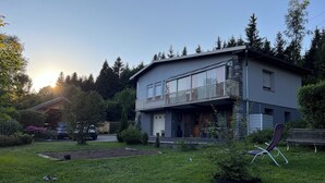 A two-story house with a balcony, surrounded by a garden and trees.