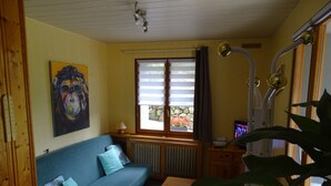 A cozy room with a blue sofa, a wooden table, a radiator, a window with curtains, a painting, and a television.