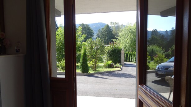 An open door leading to a parking area with a view of a green landscape and trees.