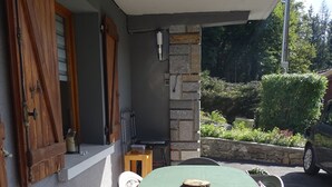 A covered patio with a round table and chairs, a stone wall, and a wooden door with shutters.