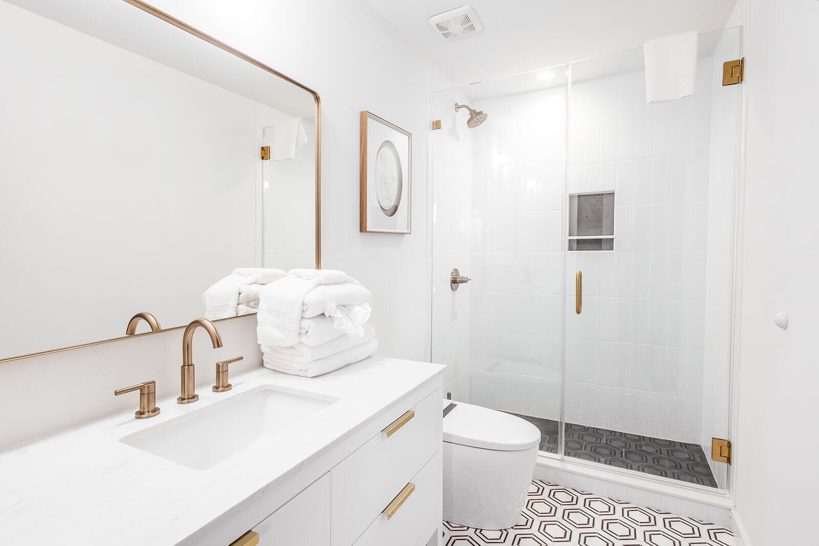Un baño moderno con lavamanos blanco, accesorios dorados, un cuadro enmarcado y una zona de ducha.