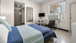 Une chambre d’hôtel avec un lit, un bureau, une chaise, une télévision et un miroir.