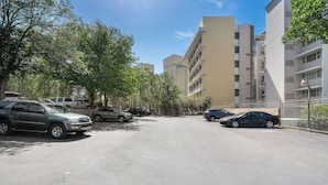 Un parking avec plusieurs voitures, des arbres et, au fond, un immeuble à plusieurs étages.