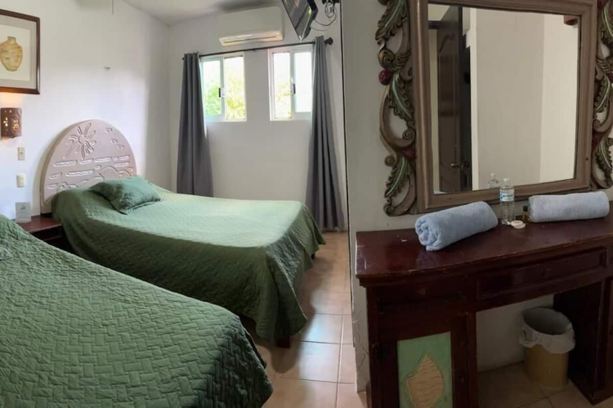 A room with two beds, a wooden dresser, a mirror, and a window with curtains.