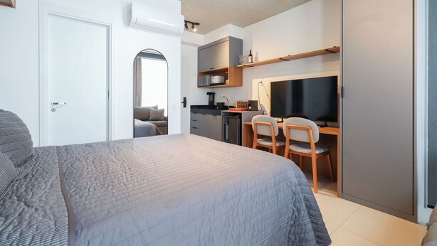 A compact bedroom with a bed, a desk, and a kitchenette. - Flat Moderno Perto do Metr e do Parque Ibirapuera (São Paulo)