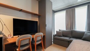 A modern hotel room with a large bed, a sofa, a TV, and a desk with two chairs. - Flat Moderno Perto do Metr e do Parque Ibirapuera (São Paulo)