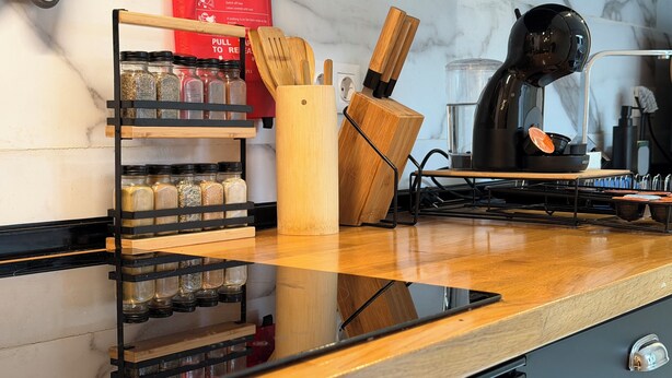 A kitchen counter with a spice rack, wooden utensils, and a coffee machine.