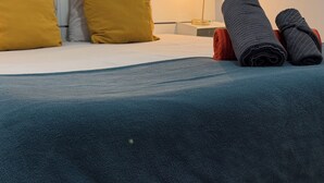 A neatly made bed with a blue blanket, two rolled-up towels, and two pillows in a modern hotel room.