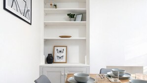 Ein Essbereich mit einem Holztisch, der für vier Personen gedeckt ist, weißen Schränken und einem Wandregal mit Dekorationen.