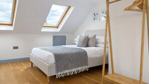 Ein modernes Schlafzimmer mit Dachfenster, einem Holzschrank und einem Bett mit grauer Decke.