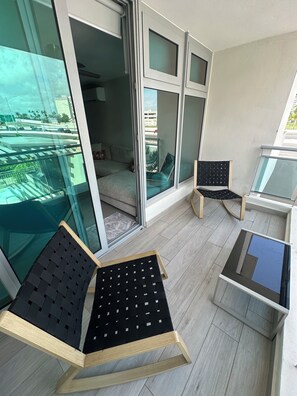 Un balcon équipé de deux fauteuils, d  ’une petite table et d’une porte-fenêtre coulissante donnant sur un espace de vie intérieur.