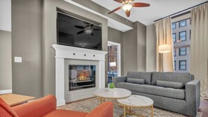 A modern living room with a fireplace, a grey sofa, an orange armchair, and a ceiling fan. - Central Downtown Loft FREE Parking•Gym•Security (Cleveland)