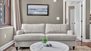 Una sala de estar con un sofá seccional color beige, una mesa de centro de mármol y un cuadro en la pared.