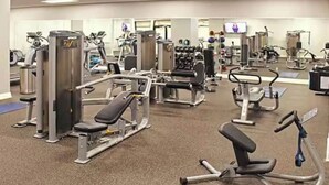 Un gimnasio con diferentes máquinas de ejercicio, espejos y una pantalla de televisión.