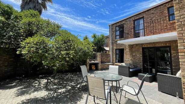 Un bâtiment moderne à deux étages, doté d’une façade en briques, d’un espace extérieur aménagé avec une table et des chaises en verre, et d’un patio avec un foyer.