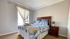 Une chambre à coucher avec un grand lit, une table de chevet, une tête de lit en bois et une fenêtre avec des rideaux.