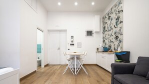 A modern living room with a sofa, a dining table with chairs, a kitchen area, and a bathroom visible through an open door. - CasaRÉ - One Bedroom Guest House, Sleeps 2 (Naples)