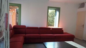 A red sectional sofa, a small table, and a window with a view of greenery.
