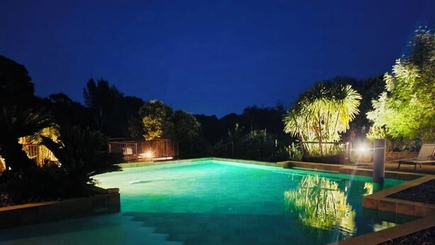 A nighttime view of a swimming pool with surrounding trees and a well-lit deck area.