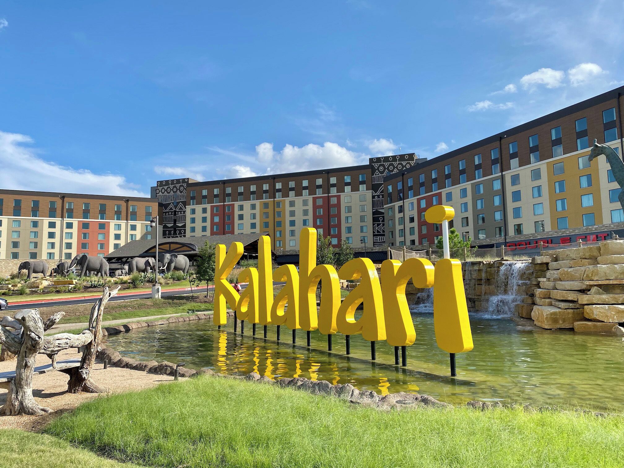 A hotel with a large sign reading "Kalahaari" in front of a water feature and a building with multiple windows in the background.
