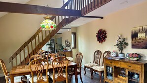 Un comedor con una mesa y sillas de madera, una escalera y un armario con puertas de cristal.